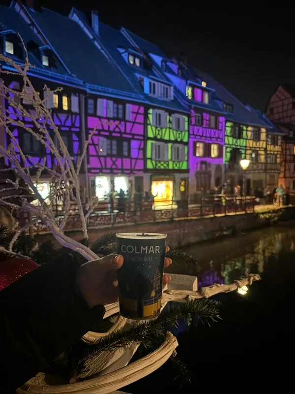 Casas iluminadas con vaso de vino caliente en Colmar, Alsacia
